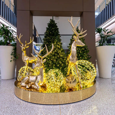 Decorative display of illuminated deer figures in a modern indoor setting with plants and a Christmas tree.
